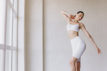 Sporty young woman with slim body doing yoga practice at modern room with panoramic windows - concept of healthy life and natural balance between body and mental development