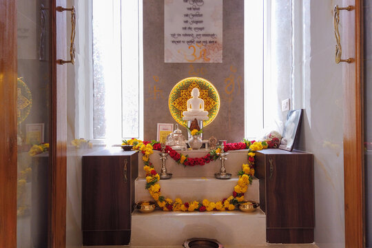 A Divine view of a Hindu Pooja room dedicated to Lord Mahavira and decorated with floral gardens and oil lamps in India.