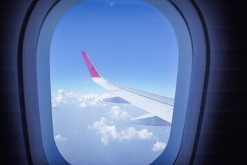 A Window view of an Airplane Wing gliding smoothly against the silvery clouds and blue sky in India.
