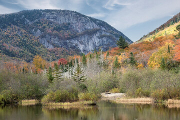 Naklejka premium Autumn in the scenic White Mountains of New Hampshire. Colorful fall foliage and steep cliff face of Mount Willard viewed from Willey Pond in Crawford Notch State Park.