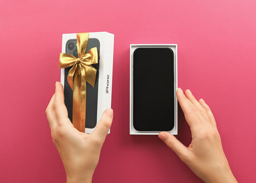 woman opens a gift box with a new iPhone in it on a purple background, top view. New Year, Valentines day, birthday gifts concept
