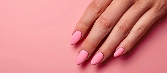 Fototapeta premium Manicured hand with pink matte nails on a pink background in a beauty salon emphasizing copy space image