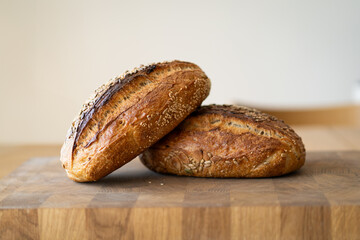 Two loaves of sourdough bread, freshly baked and still warm, are stacked on a wooden surface. The...