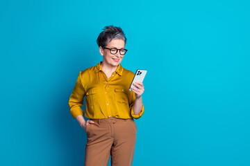 Photo of pretty cheerful woman wear shirt spectacles chatting apple iphone samsung device emtpy space isolated blue color background