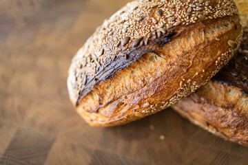 Two loaves of sourdough bread, freshly baked and still warm, are stacked on a wooden surface. The...