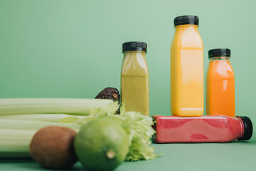 Fruit and vegetable smoothies in transparent plastic bottles. Green, red, orange smoothies on a green background. The concept of healthy eating. Front view