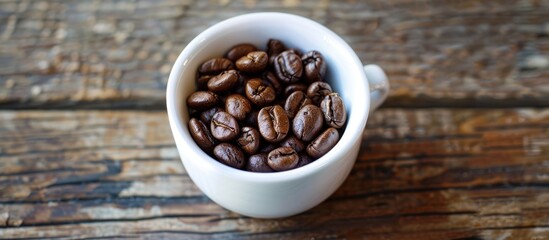Fototapeta premium A white cup filled with roasted coffee beans on a wooden surface makes an ideal copy space image
