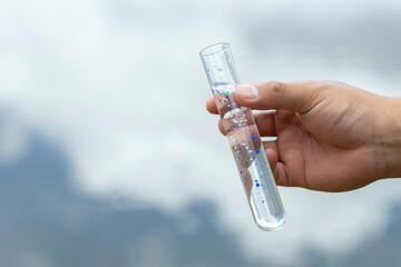 Microplastics. Male hands holding a test tube containing microplastic fragments and dirt on a lake....