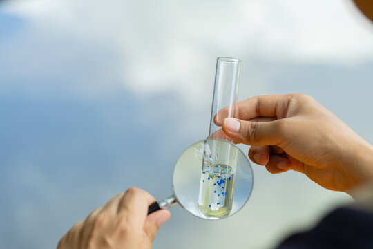 Microplastics. Male hands holding a magnifying glass to check for pollution in water contained in a test tube. test tube containing microplastic fragments and dirt on a lake. plastic pollution.