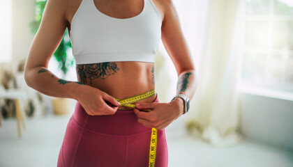 Young slim strong sporty athletic fitness trainer instructor woman in sportswear holds measure tape on waist training do exercises at home gym. Workout, sport, motivation. Female losing weight