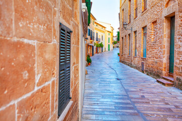 Narrow street with a brick wall on the side. The street is empty and the buildings are old. Old town of Mallorca island