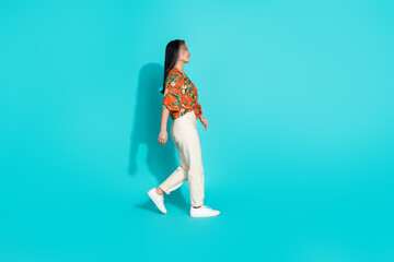 Full length photo of charming positive woman wear orange shirt looking walking empty space isolated turquoise color background