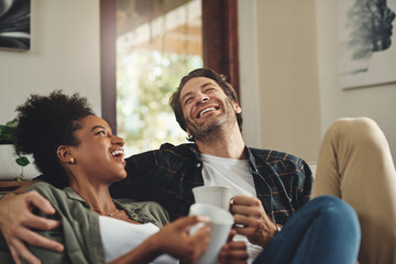 Laugh, happy couple and drinking coffee in home, talking or bonding together for love in living room. Interracial, man and funny woman in conversation for joke, story or comedy on sofa with tea cup