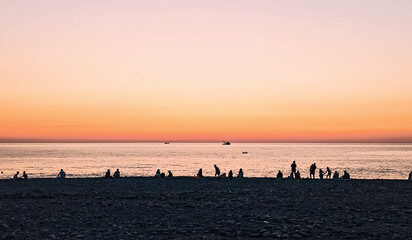 People silhouettes on pebble beach after sunset, pink horizon, clear orange sky