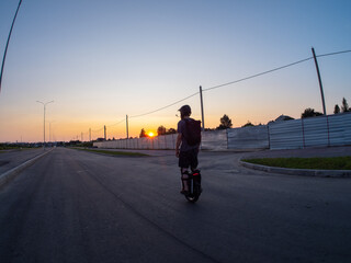 A man rides an electric monocycle on the road at sunset. Wearing a helmet and knee pads. Urban mobile transport.