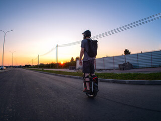 A man rides an electric monocycle on the road at sunset. Wearing a helmet and knee pads. Urban mobile transport. © pavelkant