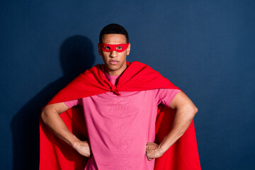 Photo of young angry superman guy in red face mask and cape fights against thieves isolated on dark...