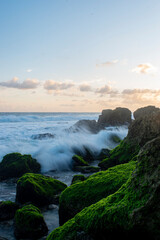 Beautiful rocky beach with green moss growing on the stones and splashing waves.