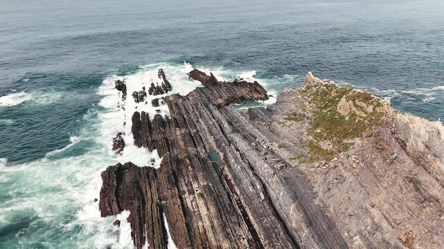Aerial footage of the huge rock washed by ocean waves. Flock of seagulls is flying beneath. Arrifana, Portugal