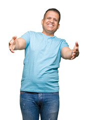 Middle age arab man wearing blue t-shirt over isolated background looking at the camera smiling with open arms for hug. Cheerful expression embracing happiness.