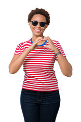 Obraz premium Beautiful young african american woman wearing sunglasses over isolated background smiling in love showing heart symbol and shape with hands. Romantic concept.