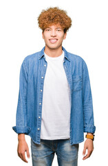Young handsome man with afro hair wearing denim jacket with a happy and cool smile on face. Lucky person.