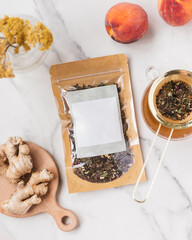 Flatlay of blank ginger peach tea packaging on marble background with fresh ginger and peaches