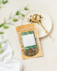 Herbal tea pouch with loose leaf tea on plate, tan tile background