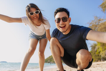 Playful asian couple lovers taking photo together at the beach, low angle.