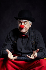 Portrait of a clown with red clown nose and bowler hat on head. Dressed in red pants and a black shirt with suspenders.