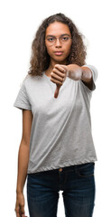 Beautiful young hispanic woman wearing glasses looking unhappy and angry showing rejection and negative with thumbs down gesture. Bad expression.