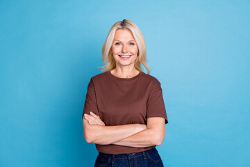 Photo of adorable nice senior woman wear trendy brown clothes crossed arms isolated on blue color...