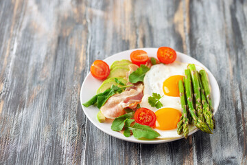 Tasty breakfast. Fried eggs with green asparagus, fried bacon on the plate on wooden table. Copy space