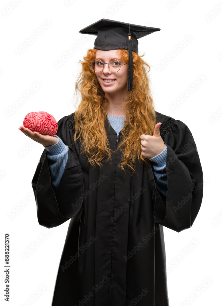 Sticker Young redhead student woman wearing graduated uniform holding brain happy with big smile doing ok sign, thumb up with fingers, excellent sign