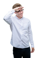 Fototapeta premium Young handsome blond man very happy and smiling looking far away with hand over head. Searching concept.