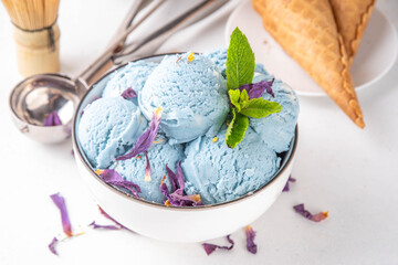 Colorful sweet butterfly pea  blue matcha scoops in portioned bowl, frozen healthy trendy sorbet dessert with waffle ice cream cones and dried butterfly pea flowers