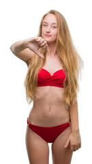 Obraz premium Blonde teenager woman wearing red bikini looking unhappy and angry showing rejection and negative with thumbs down gesture. Bad expression.