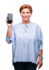 Atrractive senior caucasian redhead woman showing smartphone screen over isolated background with a happy face standing and smiling with a confident smile showing teeth