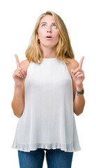 Beautiful young elegant woman over isolated background amazed and surprised looking up and pointing with fingers and raised arms.