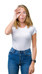 Fototapeta premium Beautiful young woman wearing casual white t-shirt over isolated background doing ok gesture shocked with surprised face, eye looking through fingers. Unbelieving expression.