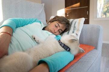 A woman and her husky puppy are seen taking a cozy nap together on a couch.