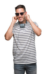 Fototapeta premium Handsome young man wearing headphones covering ears with fingers with annoyed expression for the noise of loud music. Deaf concept.