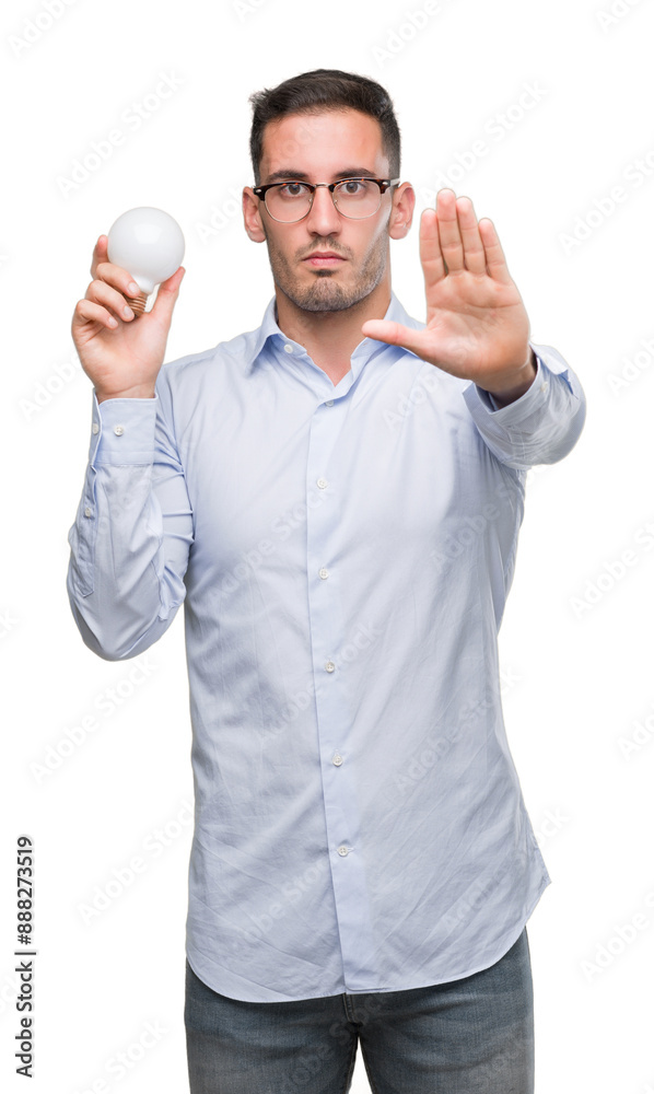 Poster handsome young man holding lightbulb as idea with open hand doing stop sign with serious and confide