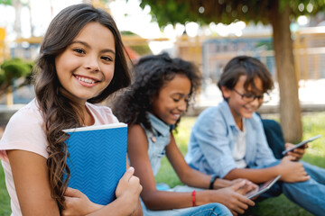 Portrait of cute little school girl and children on background with backpacks and notebooks sitting...