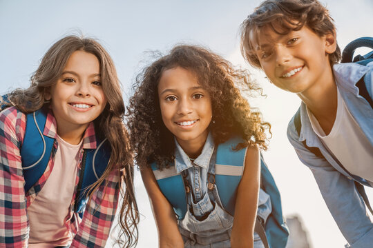 Portrait of happy multiethnic elementary middle school kids children pupils classmates friends boys and girls with backpack smiling and looking at the camera outdoors near school building