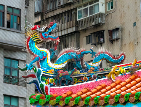Historical Longshan (Lungshan) Temple roof details in central Taipei, Taiwan, with colorful ancient drangons contrasting with urban scenery in the background