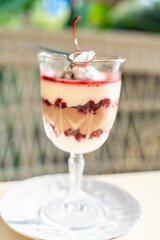 Puff cherry dessert with mascarpone cheese and whipped cream in a tall glass on the table in a cafe. Summer dessert. Exquisite presentation. Selected focus.