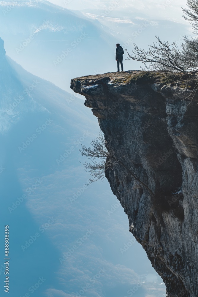 Fototapete a man stands on a cliff overlooking a valley. the scene is serene and peaceful, with the man alone o
