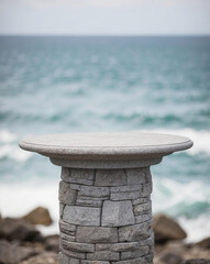 Fototapeta premium Stone podium with flat top sits on rocky shore, overlooking blue ocean with white waves. Product presentation