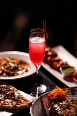 Red cocktail drink in glass on dark background with foods on table. Pizza, Pasta and Kebab platter with Cocktail.